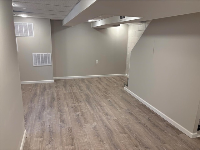 basement featuring a paneled ceiling and light hardwood / wood-style floors