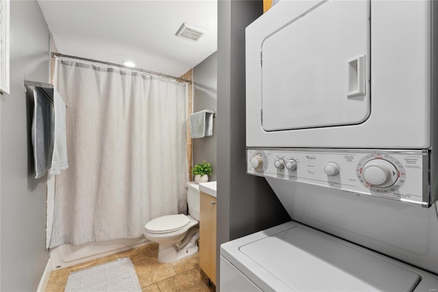 bathroom featuring stacked washer / dryer, toilet, and visible vents