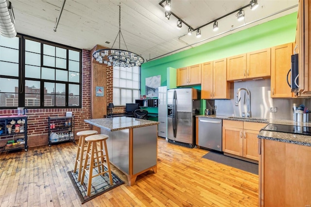 kitchen with brick wall, sink, a kitchen breakfast bar, stainless steel appliances, and light hardwood / wood-style flooring