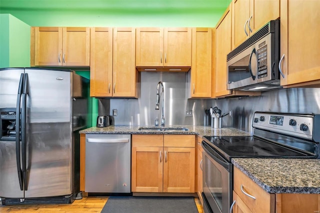 kitchen with sink, stainless steel appliances, tasteful backsplash, dark stone counters, and light wood-type flooring