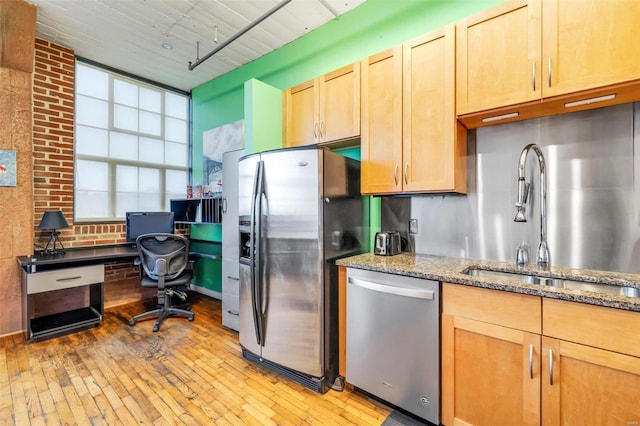 kitchen featuring appliances with stainless steel finishes, sink, light stone counters, and light hardwood / wood-style flooring