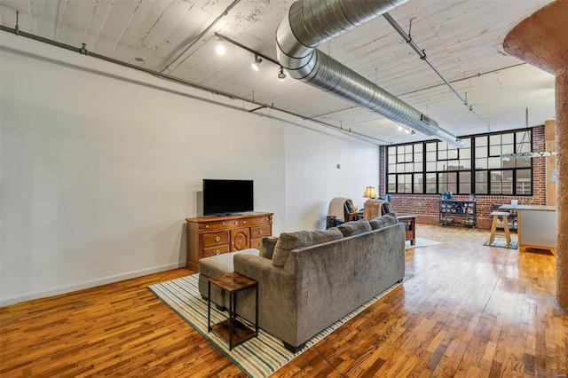 living room featuring wood-type flooring, rail lighting, and brick wall