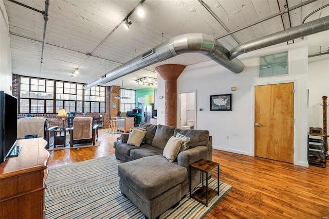 living room featuring hardwood / wood-style floors, brick wall, a high ceiling, and track lighting