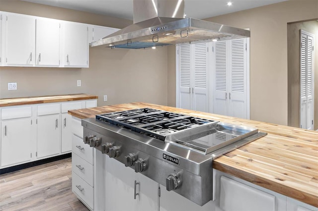 kitchen with butcher block counters, white cabinetry, island range hood, light hardwood / wood-style flooring, and stainless steel gas stovetop