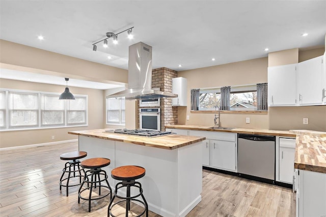 kitchen with sink, white cabinetry, wooden counters, island exhaust hood, and stainless steel appliances