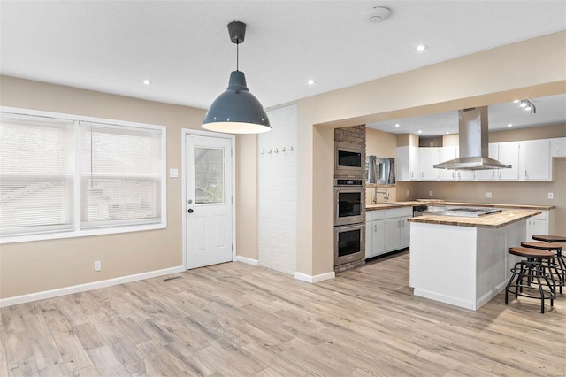 kitchen with decorative light fixtures, white cabinets, island exhaust hood, a center island, and light hardwood / wood-style flooring