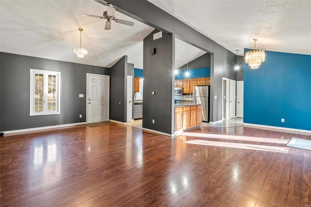 unfurnished living room featuring a textured ceiling, wood finished floors, high vaulted ceiling, baseboards, and ceiling fan with notable chandelier