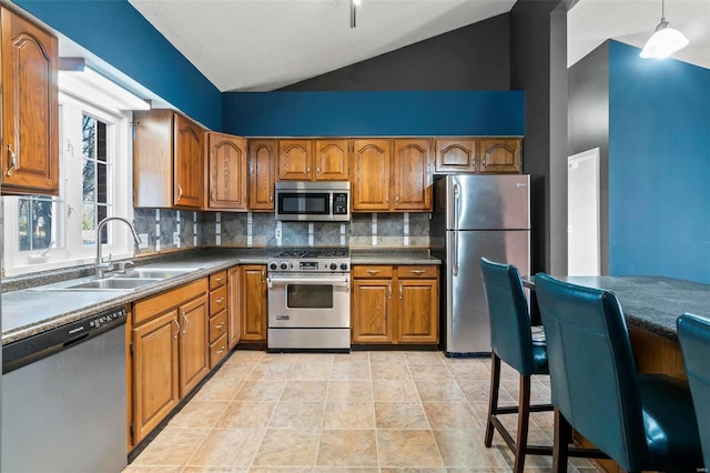 kitchen with dark countertops, appliances with stainless steel finishes, brown cabinets, decorative light fixtures, and a sink