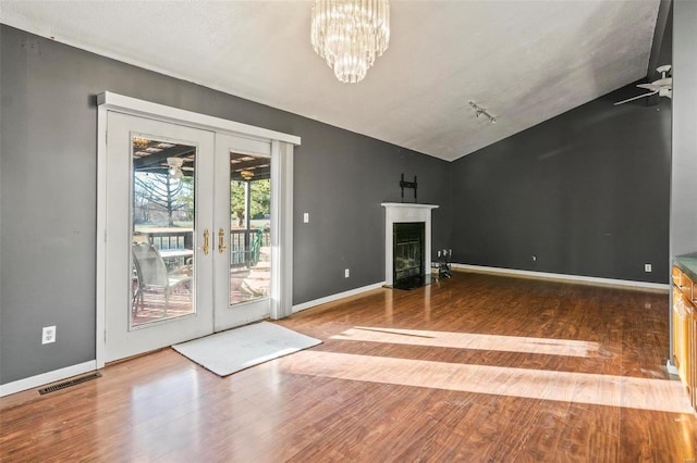 unfurnished living room with baseboards, visible vents, a fireplace with flush hearth, wood finished floors, and french doors