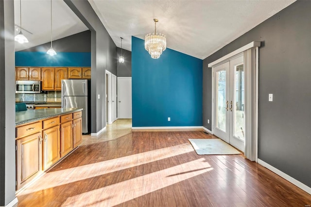 kitchen with french doors, appliances with stainless steel finishes, light wood finished floors, dark countertops, and decorative light fixtures