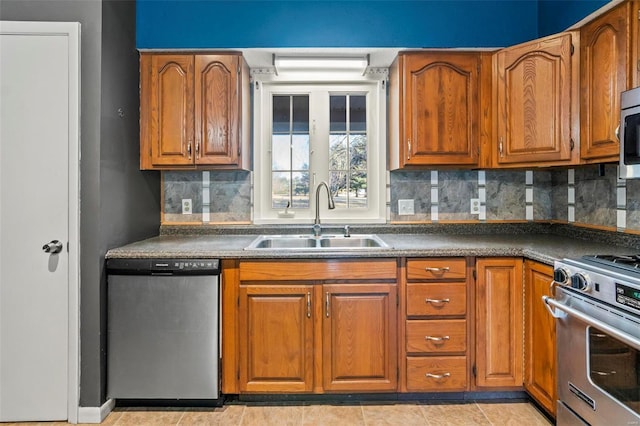 kitchen featuring a sink, appliances with stainless steel finishes, brown cabinets, tasteful backsplash, and dark countertops