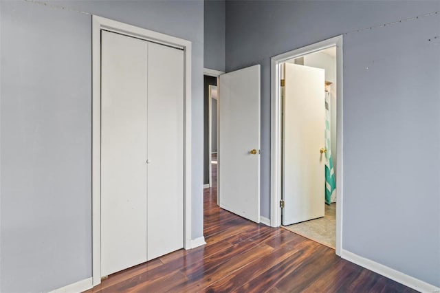 unfurnished bedroom with dark wood-type flooring, a closet, and baseboards