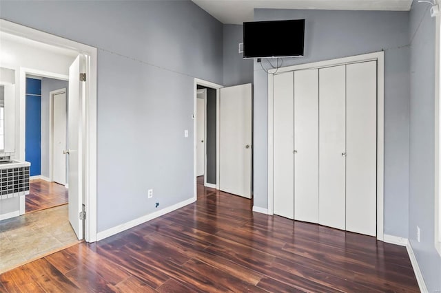 unfurnished bedroom featuring a closet, a high ceiling, dark wood finished floors, and baseboards