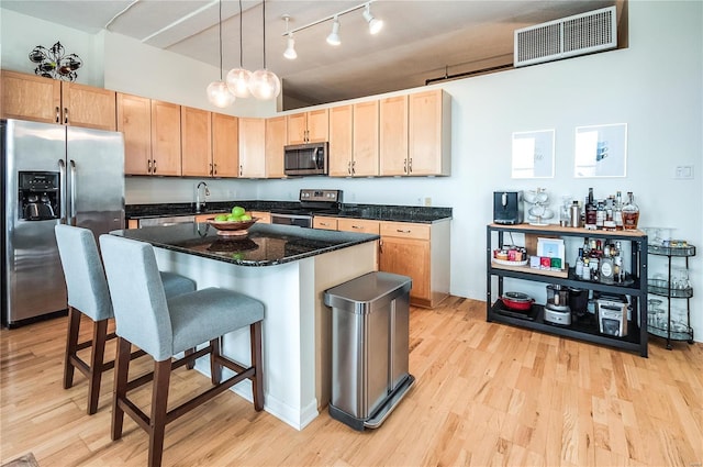 kitchen with light hardwood / wood-style flooring, hanging light fixtures, a kitchen island, and appliances with stainless steel finishes