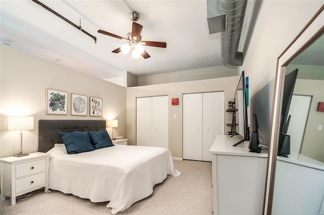 bedroom with two closets, light colored carpet, and ceiling fan