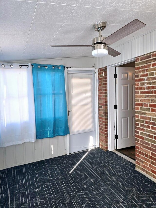 interior space featuring dark carpet, a textured ceiling, ceiling fan, and brick wall