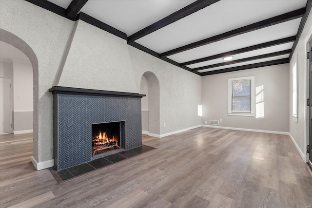 unfurnished living room featuring a tiled fireplace, hardwood / wood-style floors, and beam ceiling