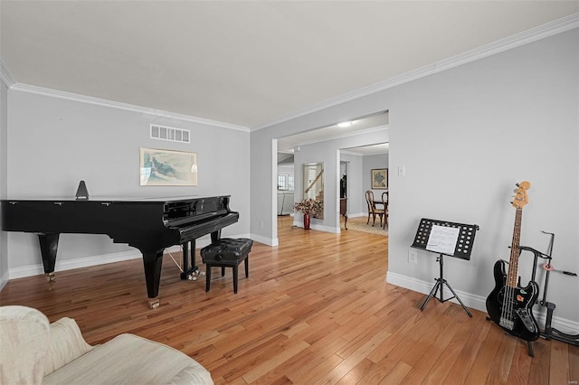 living area with visible vents, baseboards, light wood-style flooring, and crown molding