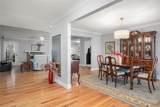 dining area with crown molding, a brick fireplace, and light wood-type flooring