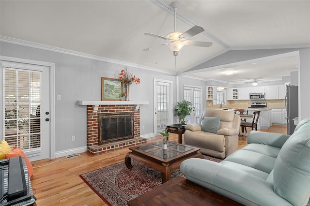 living room with a brick fireplace, crown molding, baseboards, light wood-type flooring, and lofted ceiling