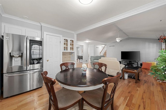 dining area featuring a ceiling fan, visible vents, light wood finished floors, stairs, and vaulted ceiling