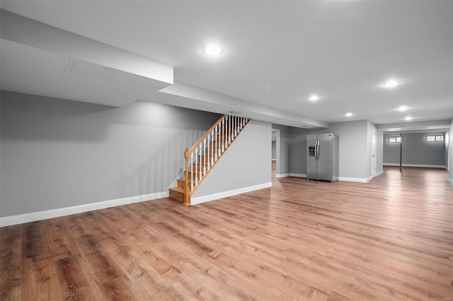 below grade area featuring baseboards, stairs, recessed lighting, light wood-style floors, and stainless steel fridge