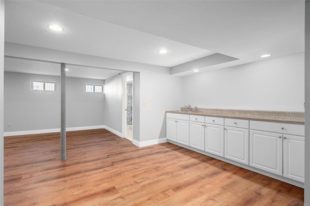 basement featuring light wood-style flooring, recessed lighting, baseboards, and a sink