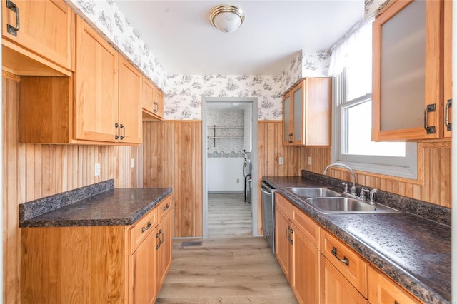 kitchen with light wood-style flooring, a sink, dark countertops, wallpapered walls, and dishwasher