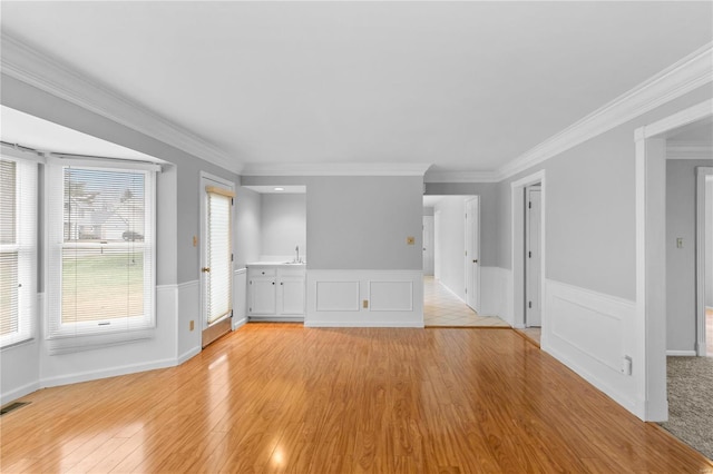 unfurnished living room featuring sink, crown molding, and light wood-type flooring