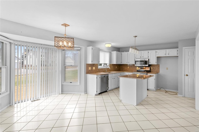 kitchen with dark stone countertops, hanging light fixtures, white cabinetry, stainless steel appliances, and a kitchen island