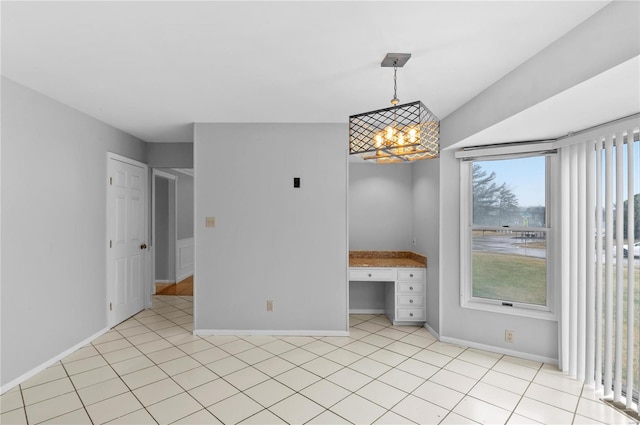 tiled empty room featuring an inviting chandelier and built in desk