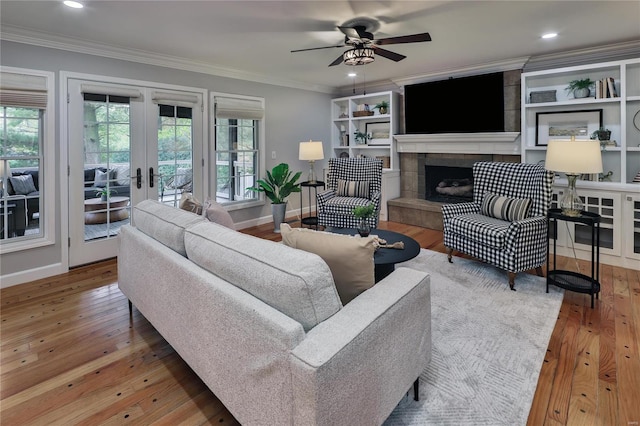 living room with a tiled fireplace, wood-type flooring, ornamental molding, and french doors