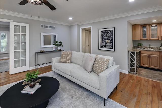 living room with ornamental molding, indoor wet bar, ceiling fan, and light hardwood / wood-style flooring