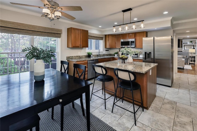 kitchen featuring appliances with stainless steel finishes, decorative light fixtures, sink, ornamental molding, and a center island