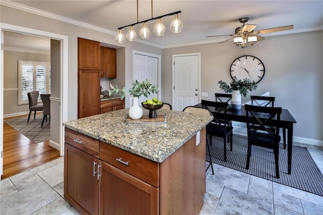 kitchen with a kitchen island, pendant lighting, ceiling fan, crown molding, and light stone countertops