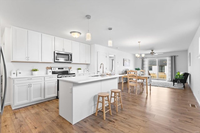 kitchen featuring a kitchen island with sink, hanging light fixtures, white cabinetry, and appliances with stainless steel finishes