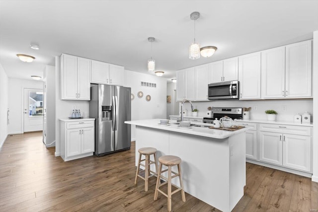 kitchen with dark hardwood / wood-style floors, pendant lighting, white cabinetry, a kitchen island with sink, and stainless steel appliances