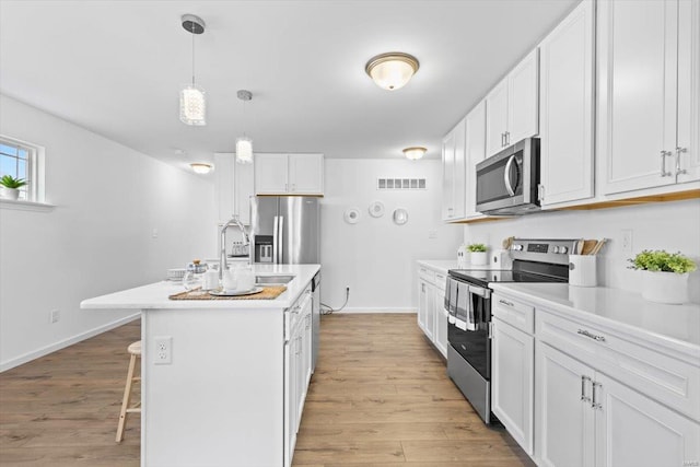 kitchen with a breakfast bar area, decorative light fixtures, stainless steel appliances, a kitchen island with sink, and white cabinets