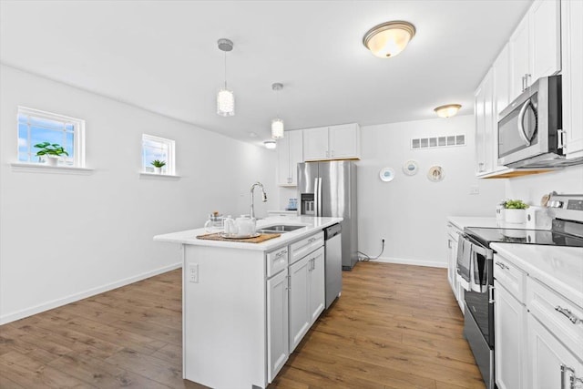 kitchen featuring hardwood / wood-style floors, an island with sink, sink, white cabinets, and stainless steel appliances