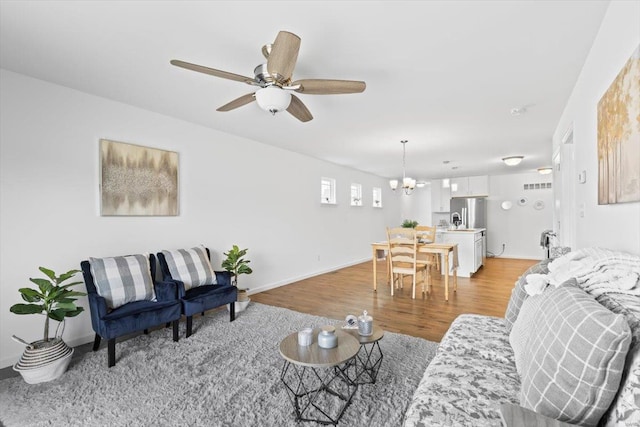 living room with ceiling fan with notable chandelier and light hardwood / wood-style flooring