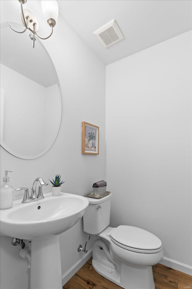 bathroom with an inviting chandelier, wood-type flooring, toilet, and sink