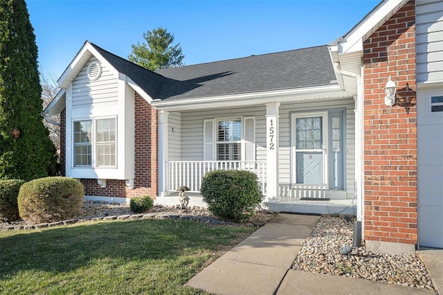 entrance to property with brick siding, covered porch, a shingled roof, and a yard