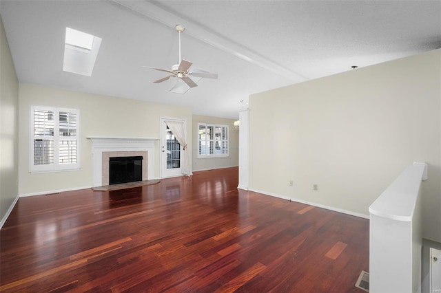 unfurnished living room featuring baseboards, vaulted ceiling with skylight, a tile fireplace, wood finished floors, and a ceiling fan