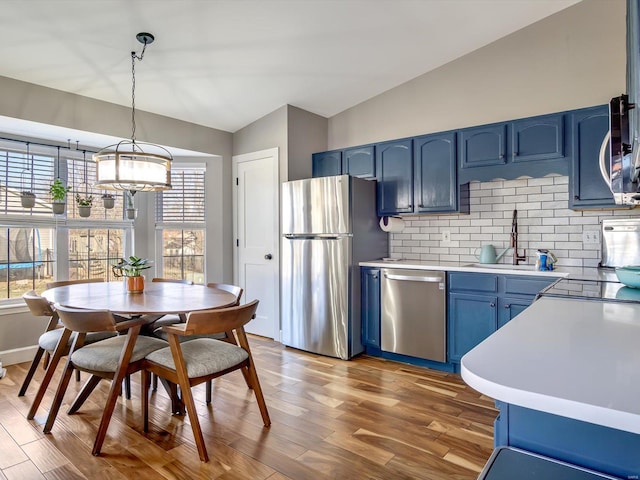 kitchen with lofted ceiling, blue cabinetry, a sink, light countertops, and appliances with stainless steel finishes