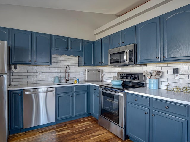 kitchen with blue cabinetry, dark wood-style flooring, a sink, vaulted ceiling, and appliances with stainless steel finishes