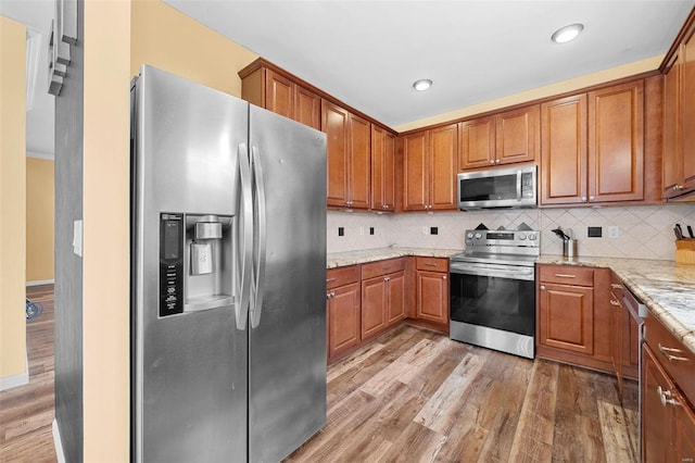 kitchen with stainless steel appliances, tasteful backsplash, light stone countertops, and hardwood / wood-style floors