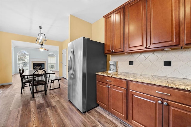 kitchen featuring tasteful backsplash, light stone counters, hanging light fixtures, dark hardwood / wood-style floors, and stainless steel fridge