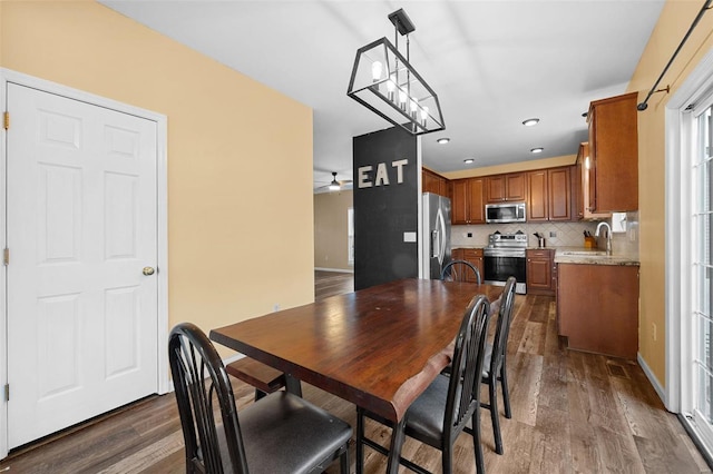 dining area featuring dark wood-type flooring, ceiling fan with notable chandelier, and sink