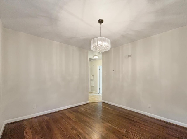 spare room featuring dark wood-type flooring and an inviting chandelier