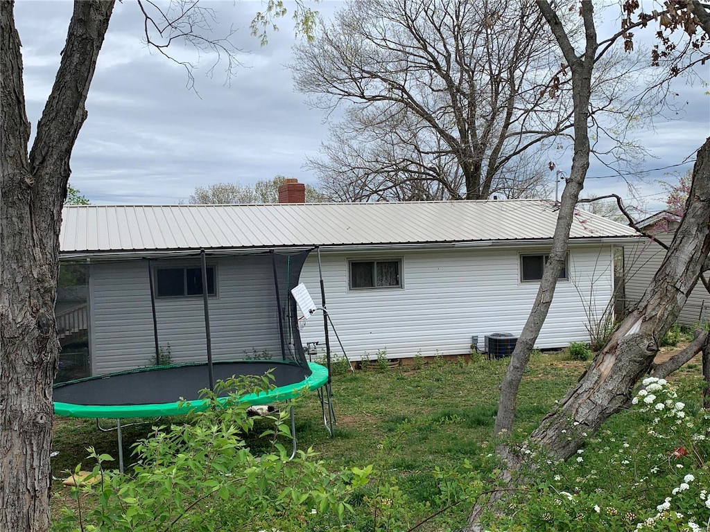 rear view of property with cooling unit, a trampoline, and a lawn